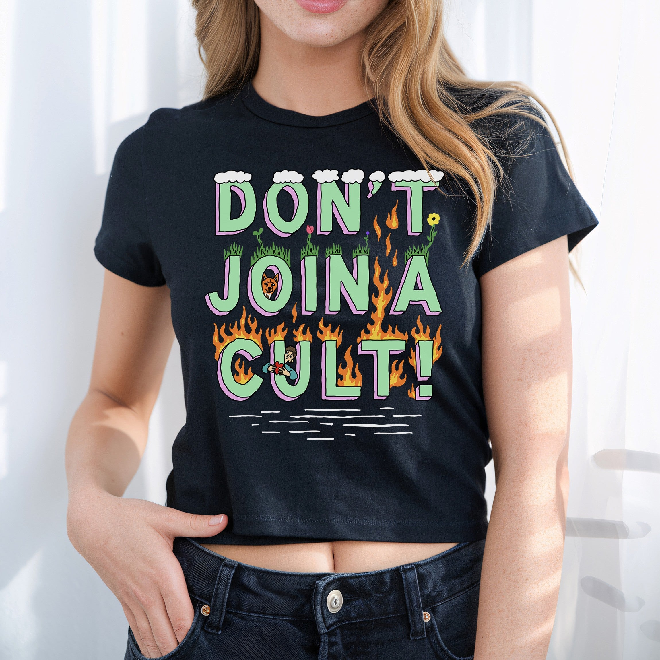 Young woman models the Don't Join A Cult Women's Baby Tee, featuring bold, stylized lettering with cartoon figures and flames, embodying a rebellious, questioning spirit against authority.