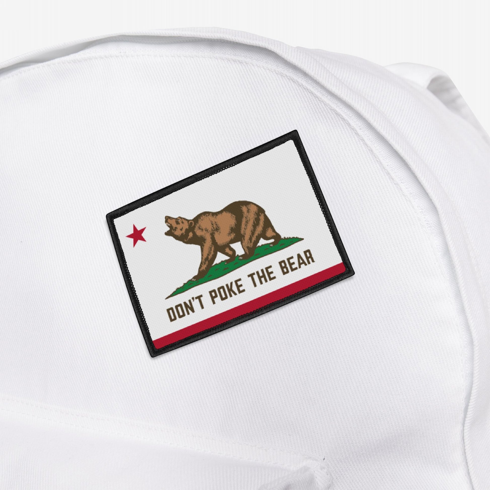 California Don't Poke The Bear Flag Patch on a white backpack, featuring a bear and red star, with the message replacing California Republic, conveying a bold statement against oppression.