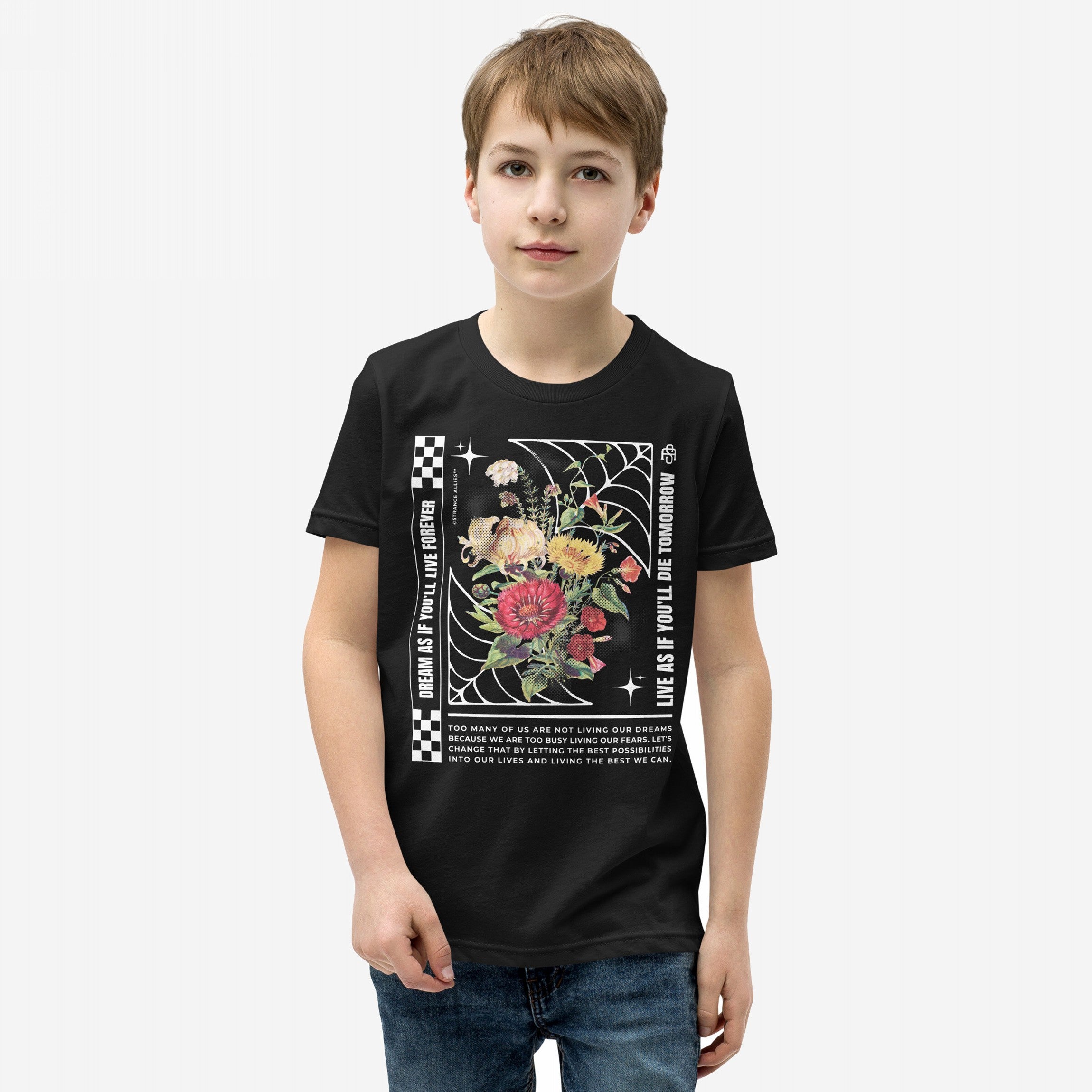 Young boy in a Dreams T-shirt featuring a vibrant floral graphic with checkerboard stripes and motivational text, embodying hope and urgency. The tee reflects an inspiring, dream-driven lifestyle.