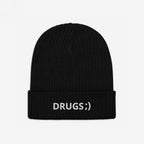 Black rib-knit beanie with “DRUGS ;)” embroidered in white on the cuff, making a bold, ironic statement. Perfect for casual wear or festivals, reflecting a playful yet edgy style.