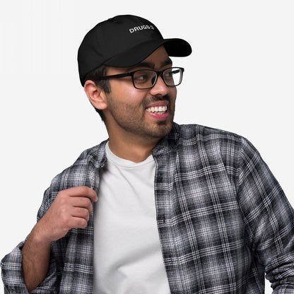 Young man wears a DRUGS :) black baseball cap with bold embroidery, paired with a casual plaid shirt and glasses, effortlessly embodying the playful, edgy vibe of the hat.