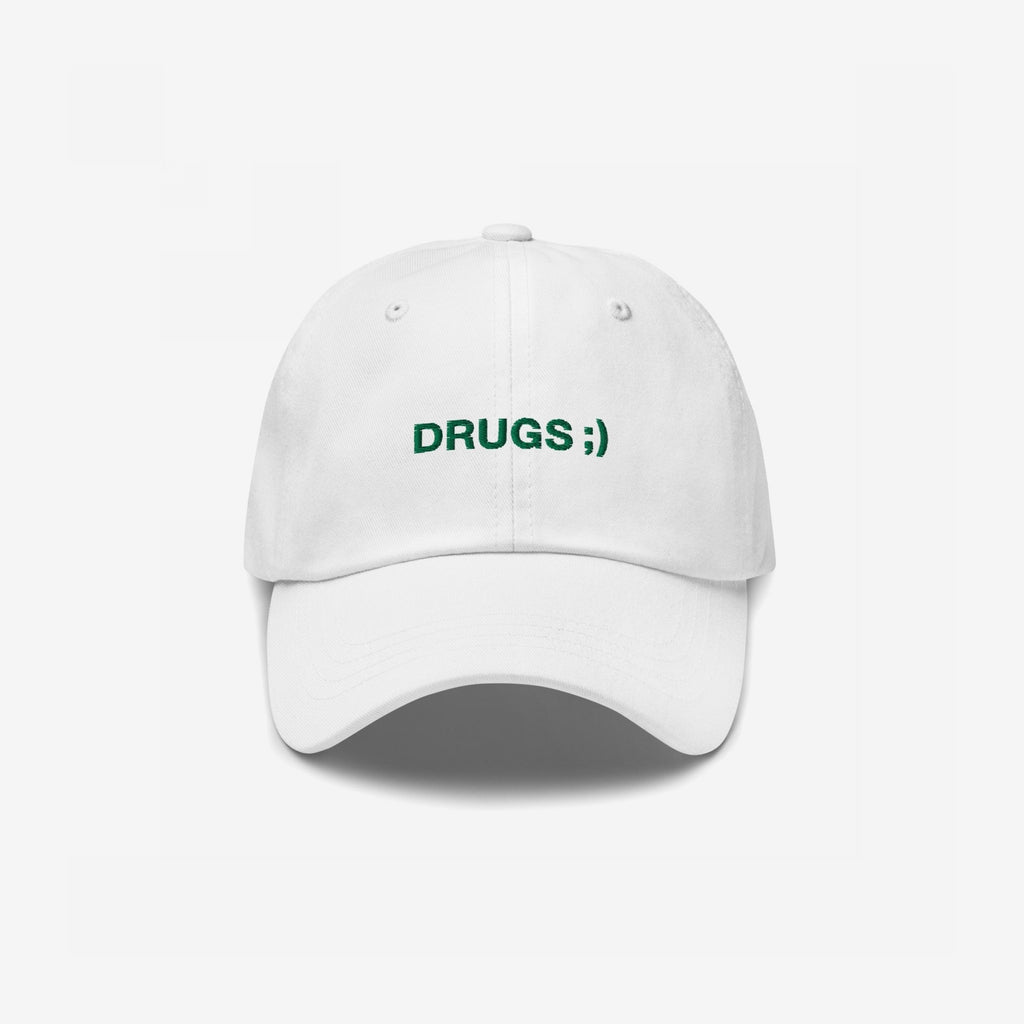 White baseball cap with DRUGS ;) embroidered in green on the front, offering a bold statement piece with minimalist flair.