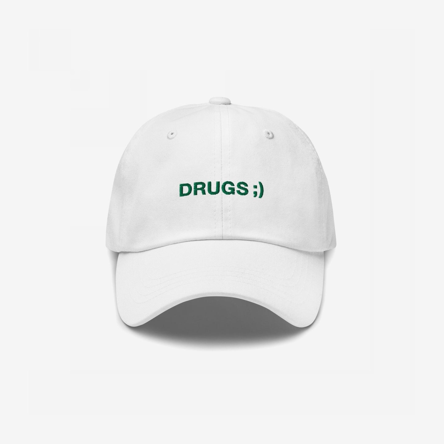 White baseball cap with DRUGS ;) embroidered in green on the front, offering a bold statement piece with minimalist flair.
