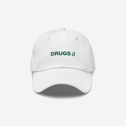 White baseball cap with DRUGS ;) embroidered in green on the front, offering a bold statement piece with minimalist flair.