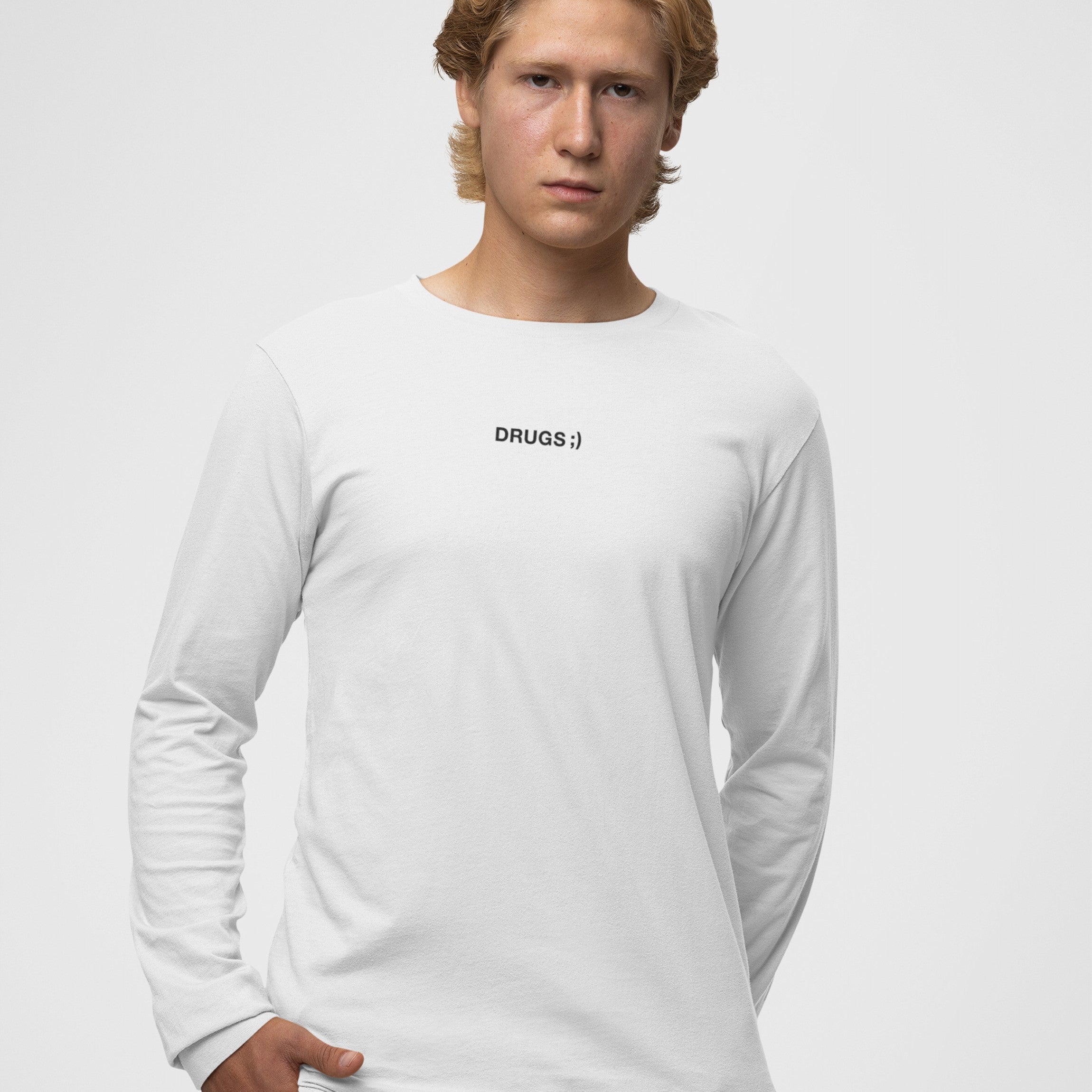 Young man wearing the Drugs T-shirt, a plain white long-sleeve shirt with DRUGS ;) in black on the chest, reflecting bold, minimalist design.