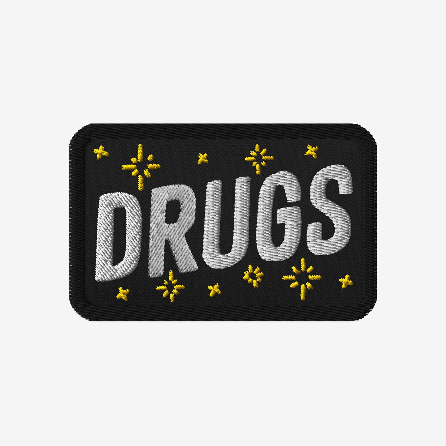 Drugs Patch featuring DRUGS in bold white stitching, adorned with small yellow star-like accents on black fabric. Perfect for expressing bold individuality and aligning with advocacy for equality and inclusivity.