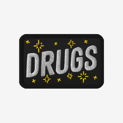 Drugs Patch featuring DRUGS in bold white stitching, adorned with small yellow star-like accents on black fabric. Perfect for expressing bold individuality and aligning with advocacy for equality and inclusivity.