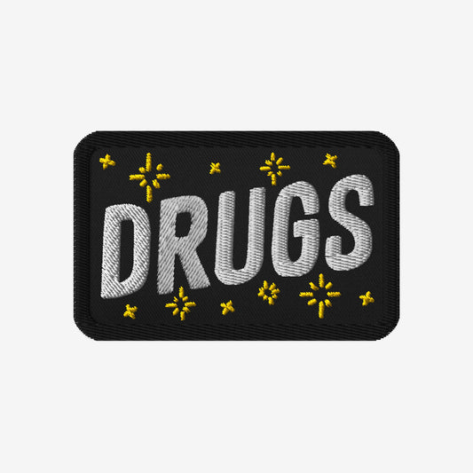 Drugs Patch featuring DRUGS in bold white stitching, adorned with small yellow star-like accents on black fabric. Perfect for expressing bold individuality and aligning with advocacy for equality and inclusivity.