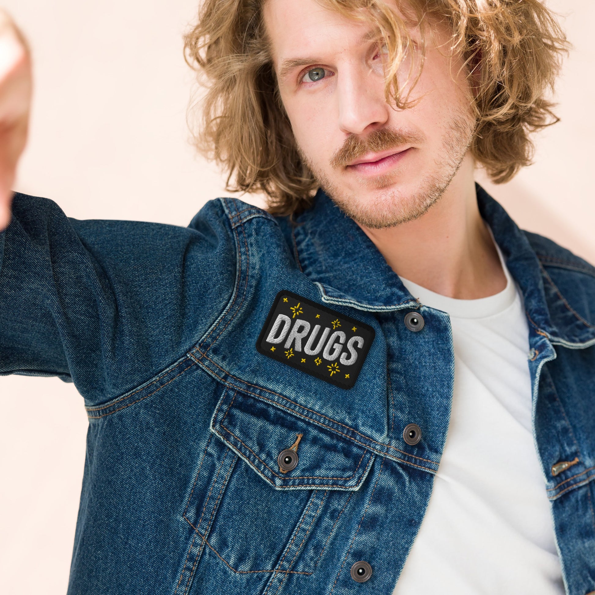 Young man wearing a denim jacket with the Drugs Patch on the chest, featuring bold block letters and starburst accents, embodying a rebellious and expressive style.