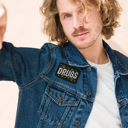 Young man wearing a denim jacket with the Drugs Patch on the chest, featuring bold block letters and starburst accents, embodying a rebellious and expressive style.