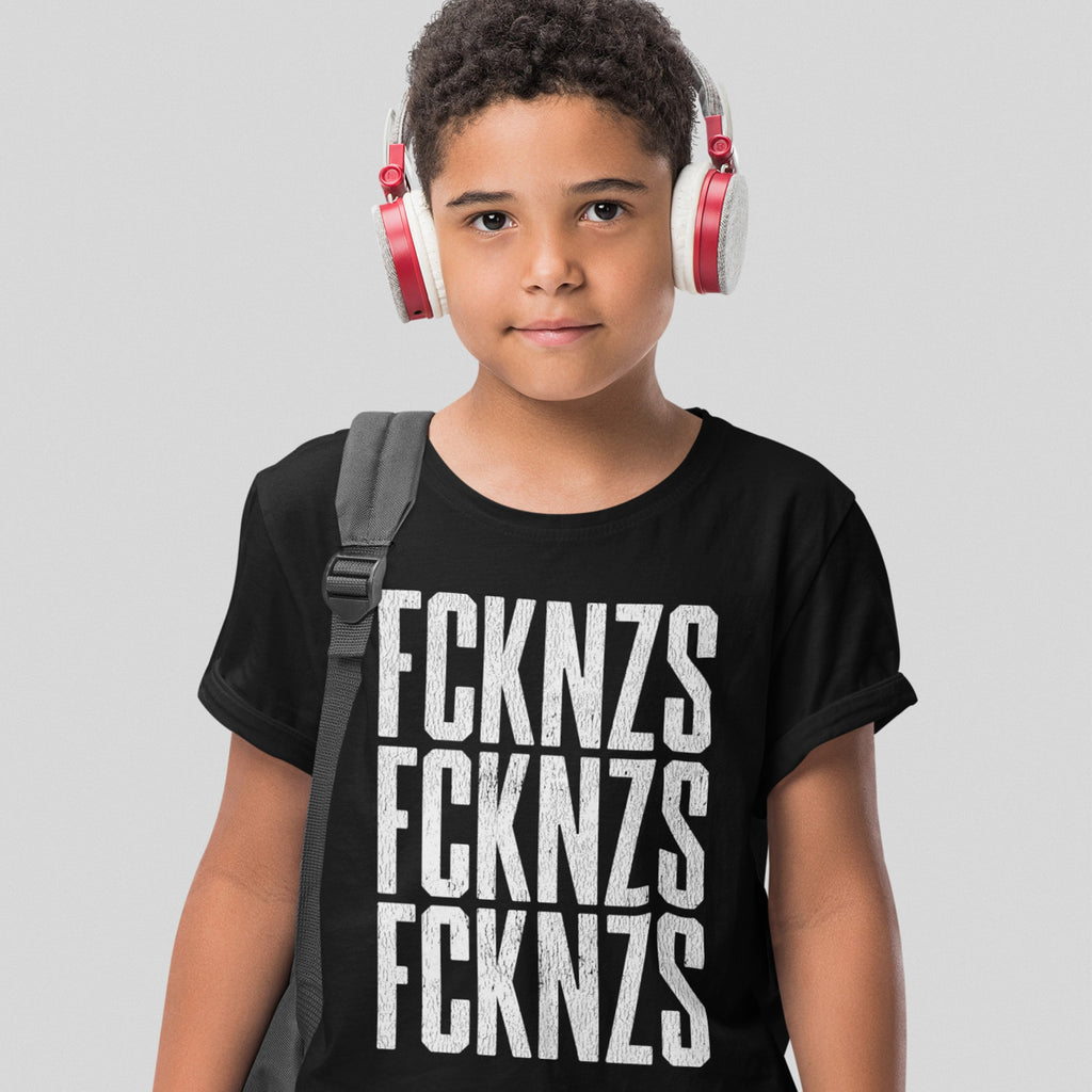 Young boy wearing a black FCKNZS T-shirt with bold white anti-fascist slogan, red-and-white headphones, and a gray backpack strap against a light gray background, embodying a stand against hate.