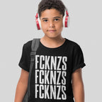 Young boy wearing a black FCKNZS T-shirt with bold white anti-fascist slogan, red-and-white headphones, and a gray backpack strap against a light gray background, embodying a stand against hate.