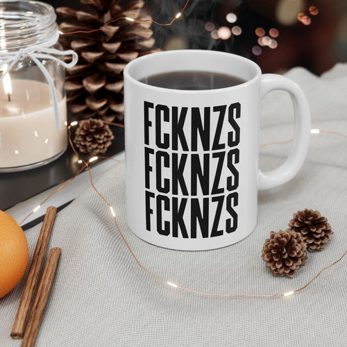 FCKNZS Mug in a cozy winter scene with lit candle, pine cones, cinnamon sticks, and fairy lights, embodying a bold anti-fascist statement.