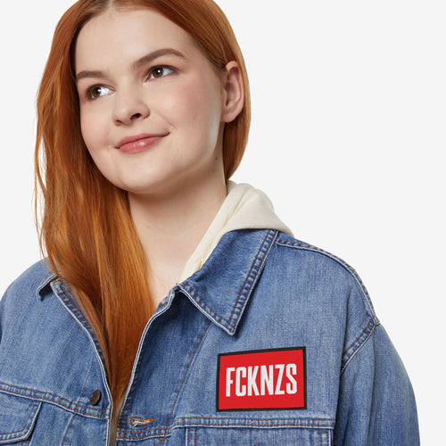 Young person wearing a light-wash denim jacket with a red FCKNZS patch, symbolizing anti-fascism and protest. The patch is bold and eye-catching, embodying a stance against hate and intolerance.