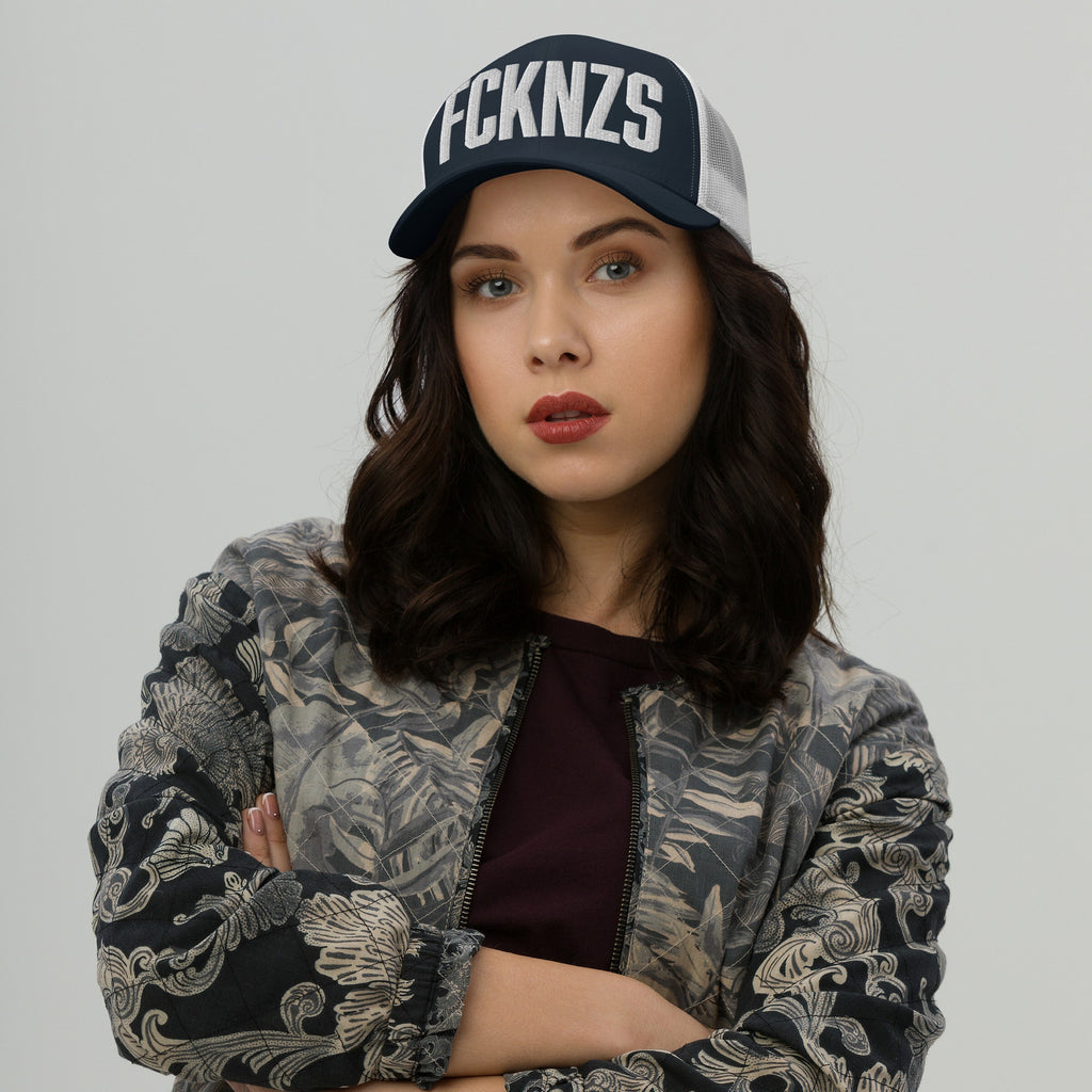 Young woman wears FCKNZS Hat, a dark trucker cap with bold white letters, embodying anti-fascist sentiment. Her confident pose complements the hat's statement, aligning with themes of equality and resistance.
