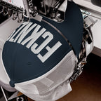 FCKNZS Hat: Automatic embroidery machine stitches white FANCY text on navy trucker cap. The anti-fascist design promotes equality, ideal for visible protest in various styles and colors.