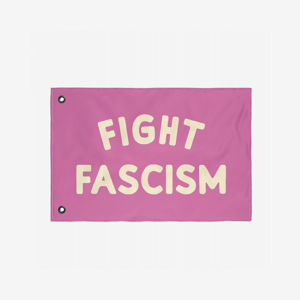 The Fight Fascism Flag features bold cream lettering on a pink fabric, ideal for protests or community events, embodying a strong anti-fascist stance with two metal grommets for easy hanging.