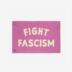 The Fight Fascism Flag features bold cream lettering on a pink fabric, ideal for protests or community events, embodying a strong anti-fascist stance with two metal grommets for easy hanging.