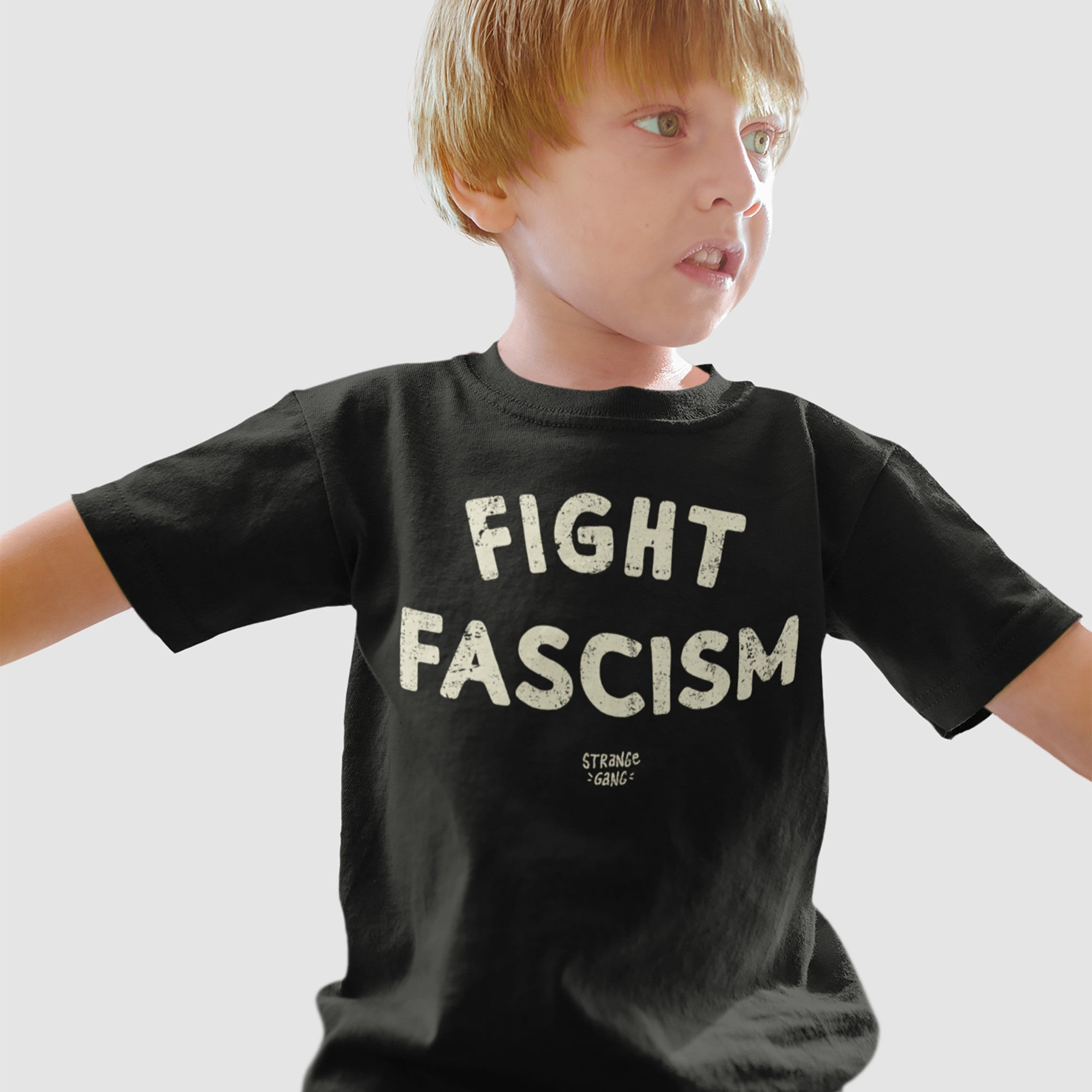 Young boy wearing a Fight Fascism T-shirt with bold off-white distressed letters. This anti-fascist design reflects activism and resistance, ideal for those who actively oppose hate and support equality.