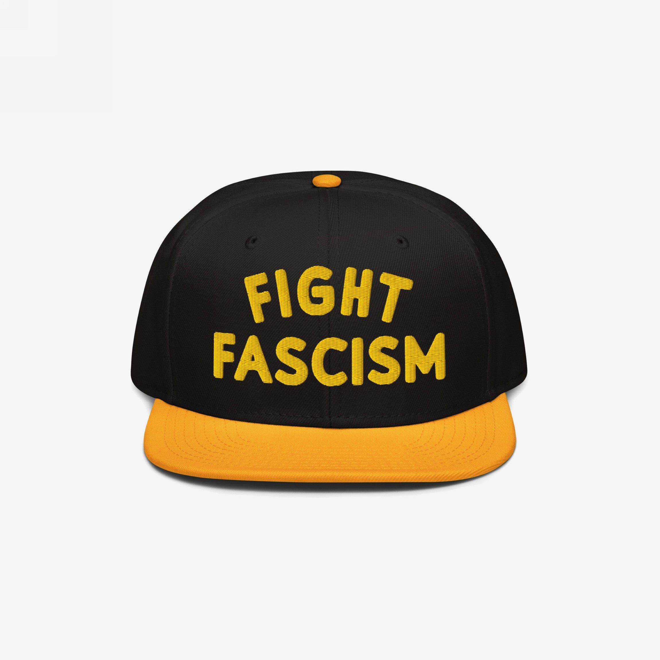 Black snapback-style cap with yellow brim and button, featuring bold yellow FIGHT FASCISM embroidery, embodying protest spirit and visibility.