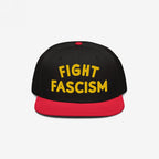 Black snapback hat with a red bill featuring bold yellow embroidery reading FIGHT FASCISM, embodying a protest spirit. Ideal for marches and daily wear to promote anti-fascist visibility.