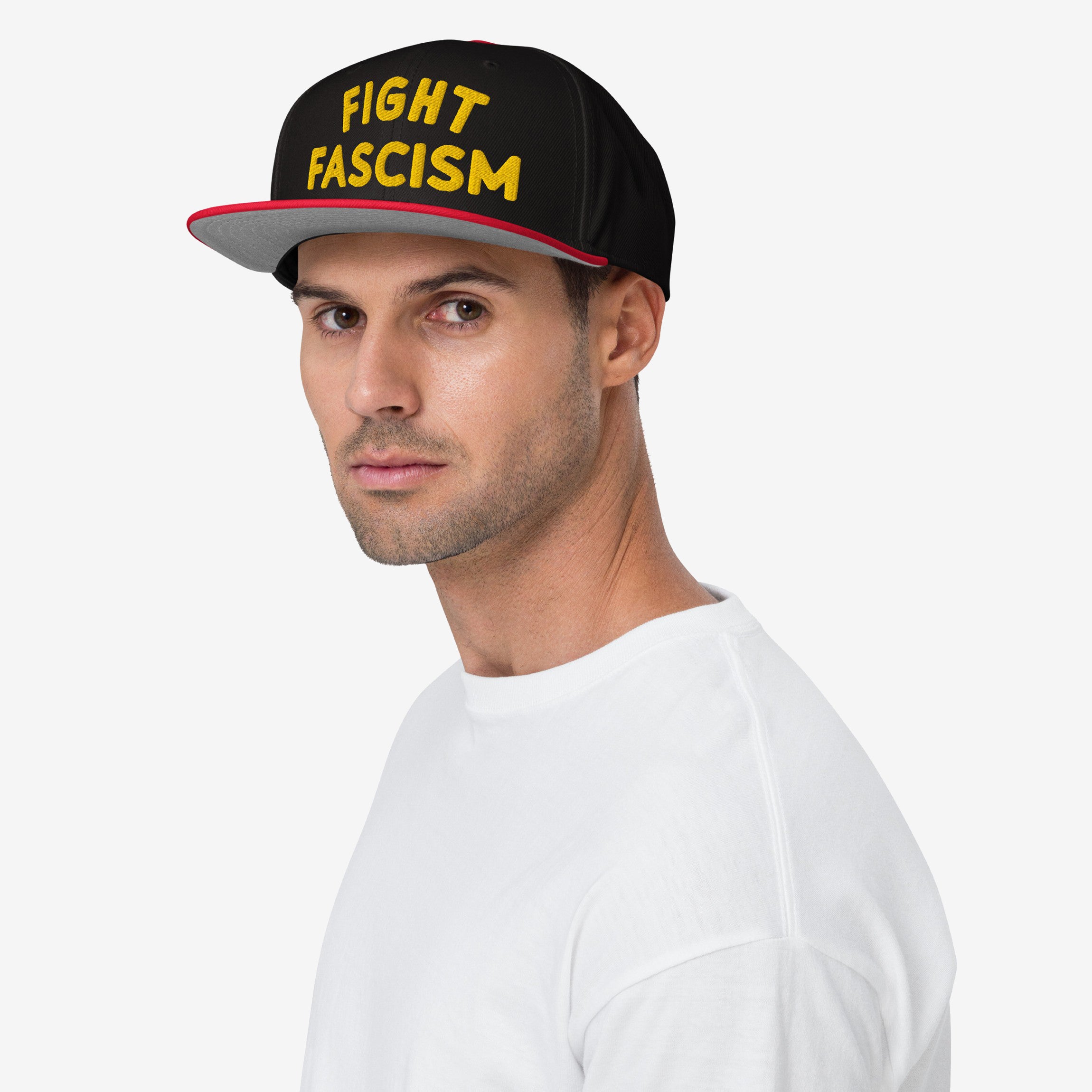 Man wearing the Fight Fascism Hat, a black cap with bold yellow embroidery, promoting anti-fascist visibility. The hat features a red underside brim, embodying a strong protest design.