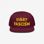 Fight Fascism Hat: A burgundy snapback cap with FIGHT FASCISM boldly embroidered in yellow, embodying protest and visibility. Ideal for marches, shows, or daily wear to promote social justice.