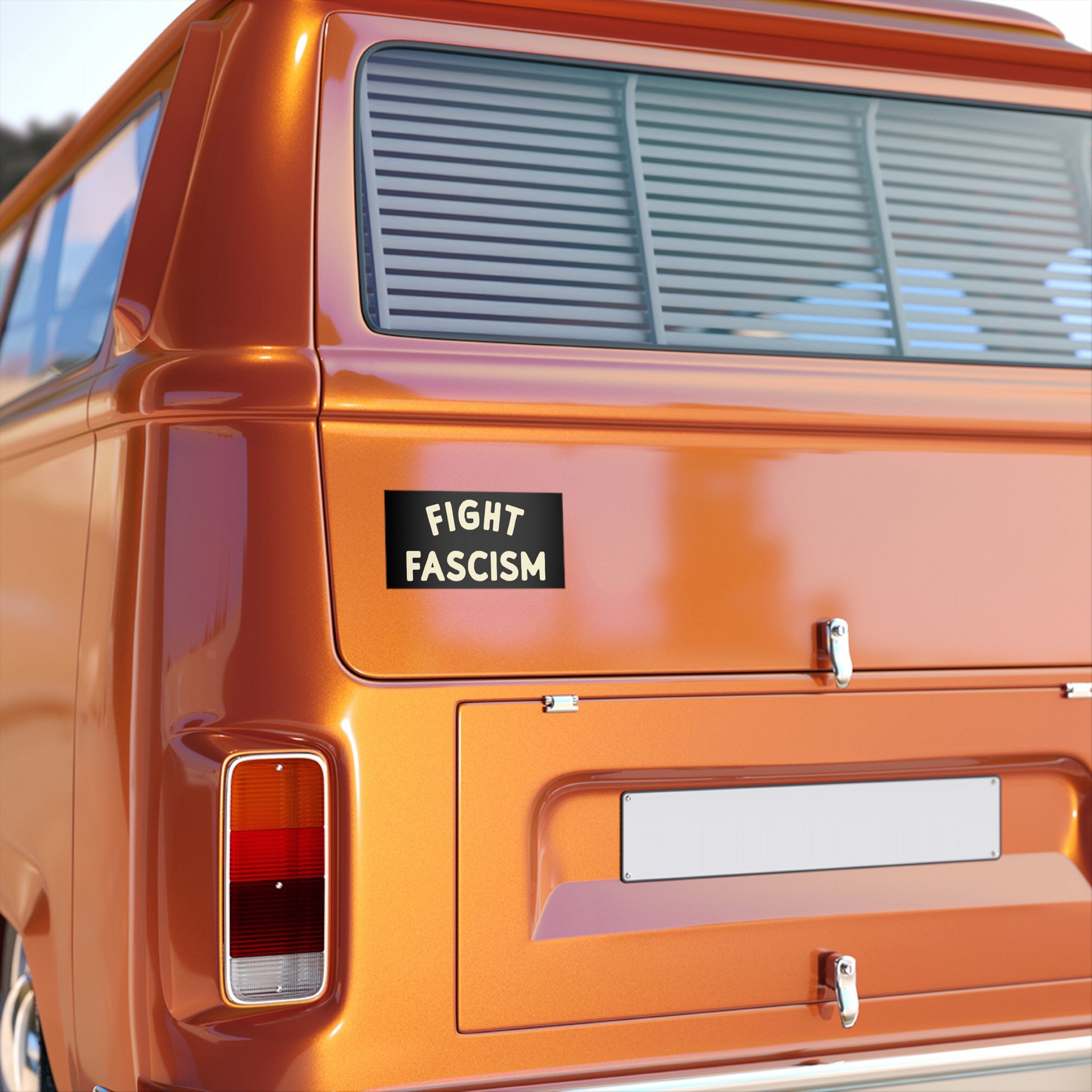 Fight Fascism Sticker & Magnet displayed on an orange van's rear, featuring bold cream lettering on black, symbolizing anti-fascist activism and equality. Ideal for vehicles and daily protest expression.
