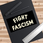 Fight Fascism Sticker & Magnet on black writing pad with digital pen and metal ruler, showcasing bold cream lettering on black, promoting anti-fascist values and equality activism.