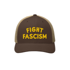 Fight Fascism Hat: Brown-and-tan mesh-back trucker style with bold yellow FIGHT FASCISM embroidery. Ideal for visible protest