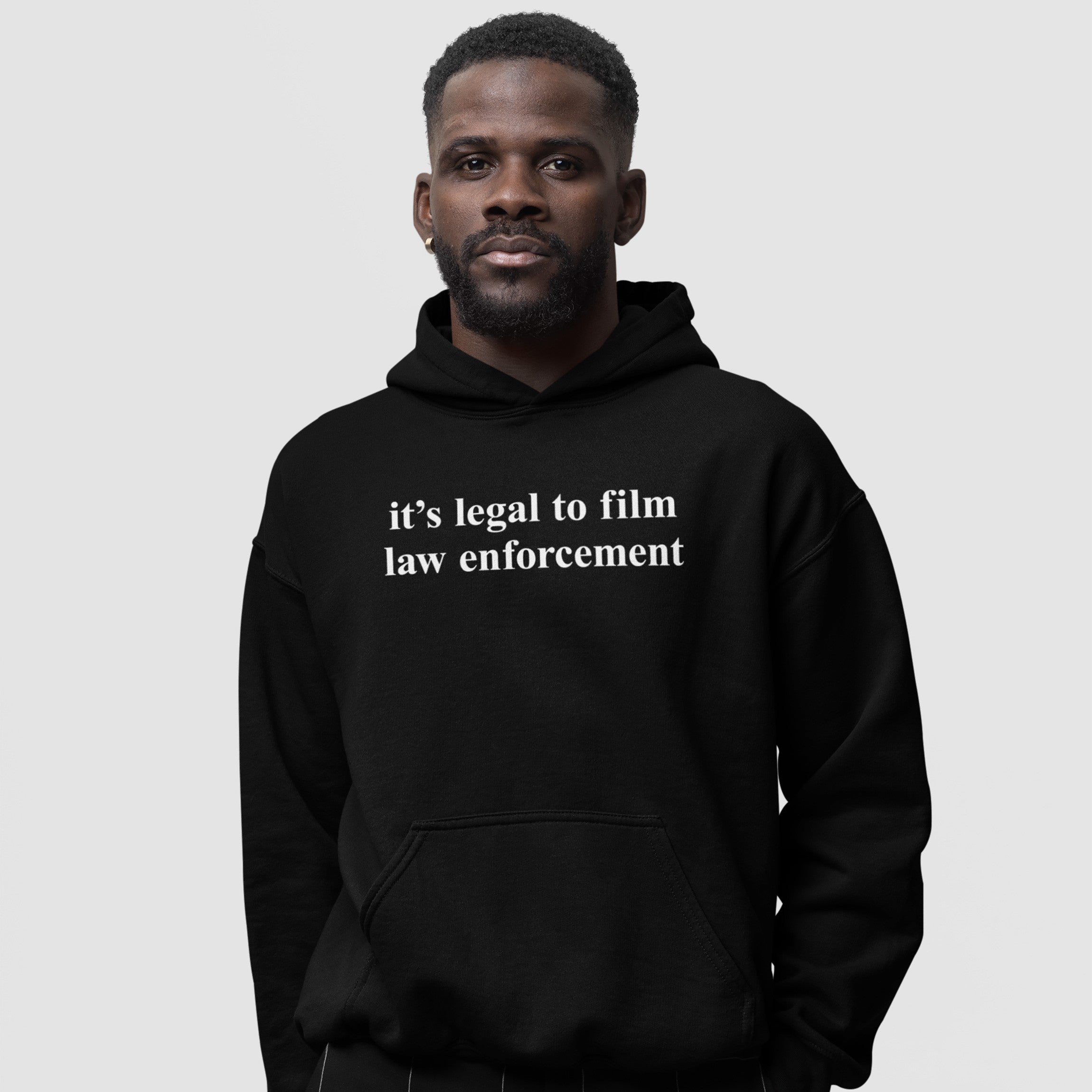 Adult male wearing a black Film The Police Hoodie & Sweatshirt with it’s legal to film law enforcement in white text, conveying a message of empowerment and social awareness.