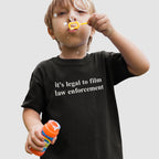 Young child wearing the Film The Police T-shirt, holding a bubble solution and wand, blowing bubbles. The shirt's message, it's legal to film law enforcement, aligns with the store’s advocacy for justice and equality.