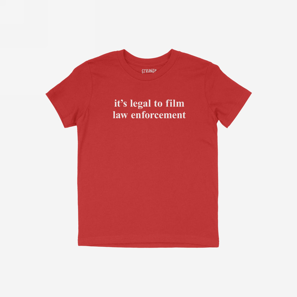 Red Film The Police T-shirt with white serif text, it's legal to film law enforcement, on front. Slightly slim fit, emphasizing activism and equality. Small inner collar label reads “STRANGE.”