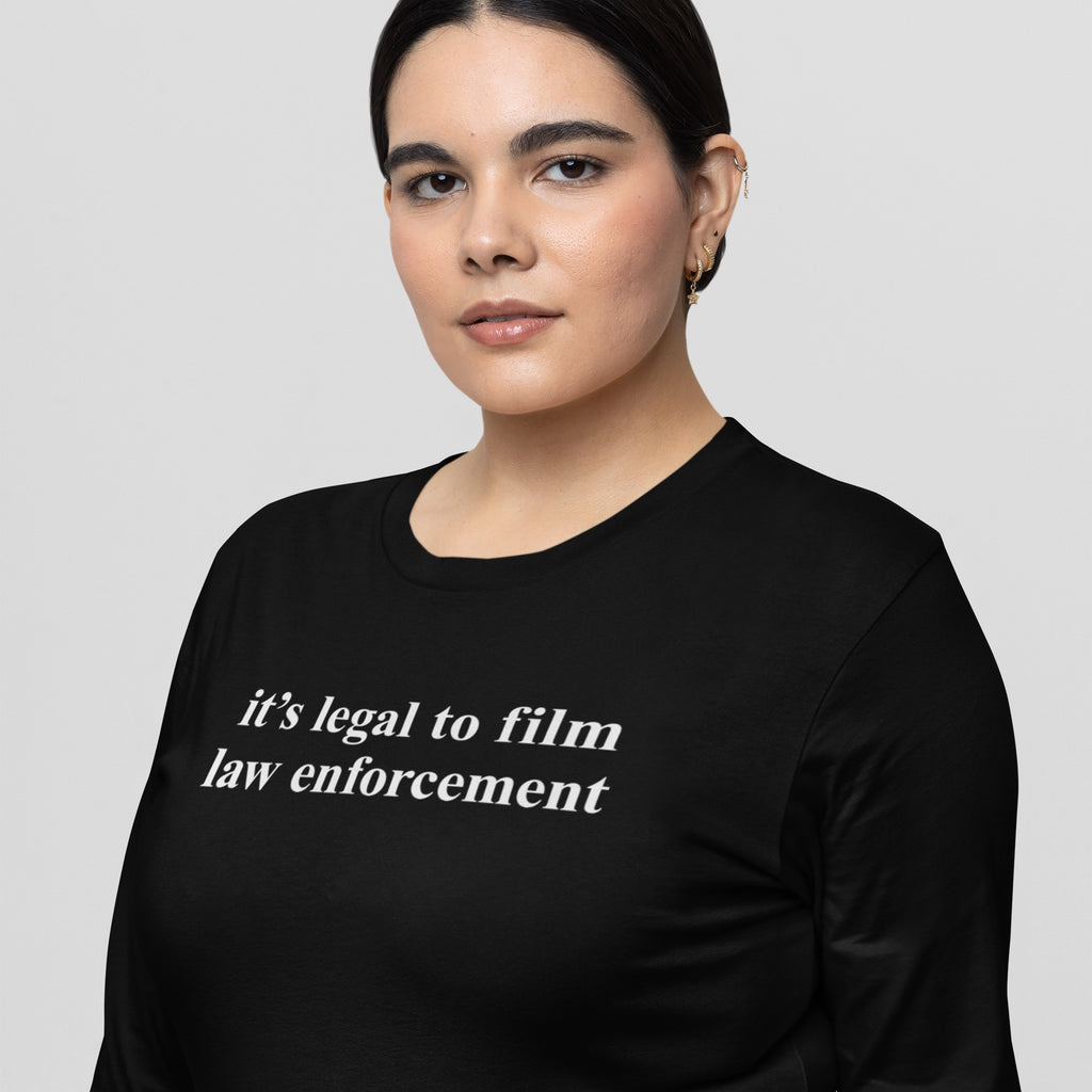 A young person wears the Film The Police T-shirt, featuring the slogan “it’s legal to film law enforcement” in white text on a black, regular fit long sleeve.