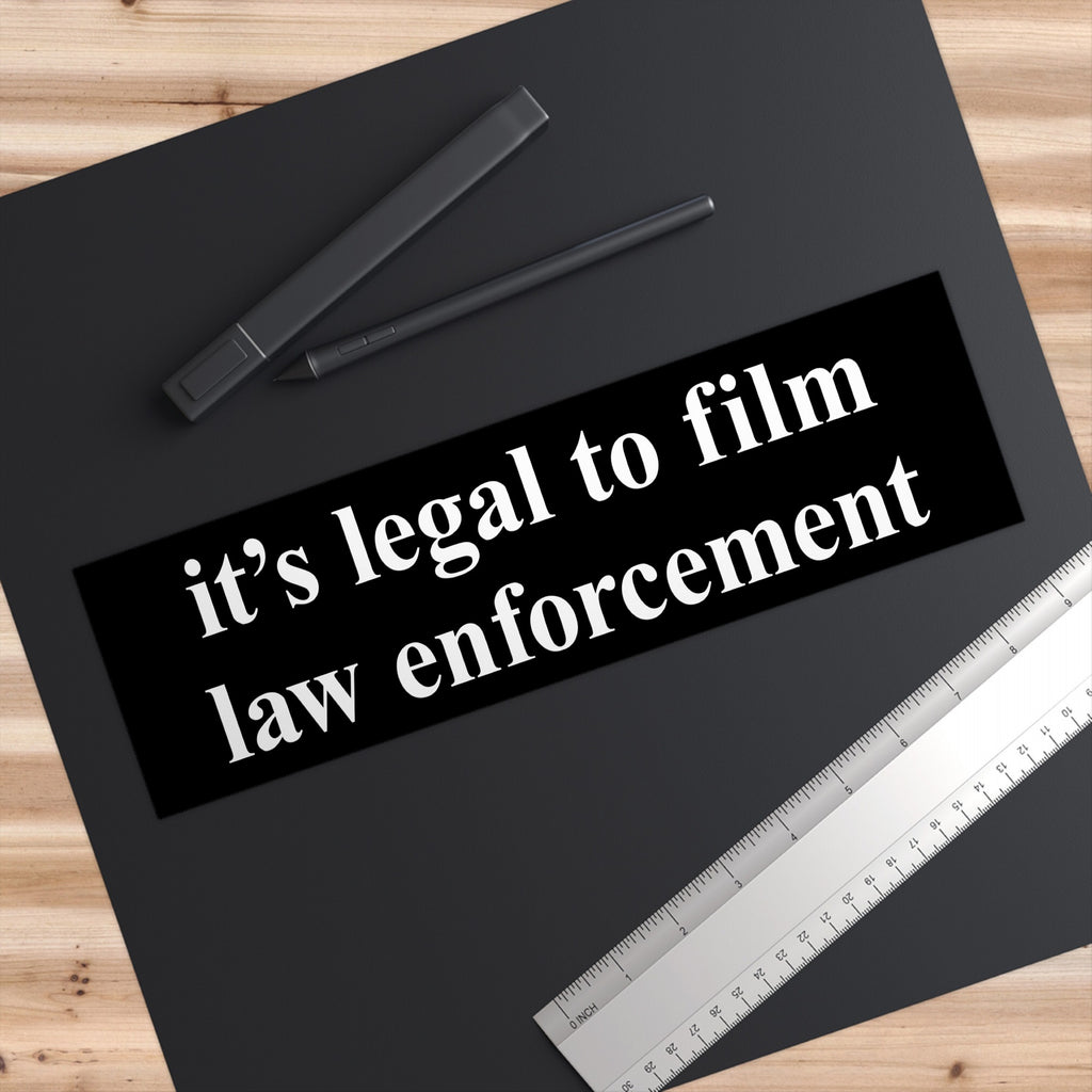 Film The Police Sticker & Magnet on a wooden desk features the bold message “it’s legal to film law enforcement” in white, accompanied by a ruler and stylus, symbolizing accountability and rights awareness.