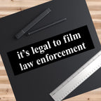 Film The Police Sticker & Magnet on a wooden desk features the bold message “it’s legal to film law enforcement” in white, accompanied by a ruler and stylus, symbolizing accountability and rights awareness.