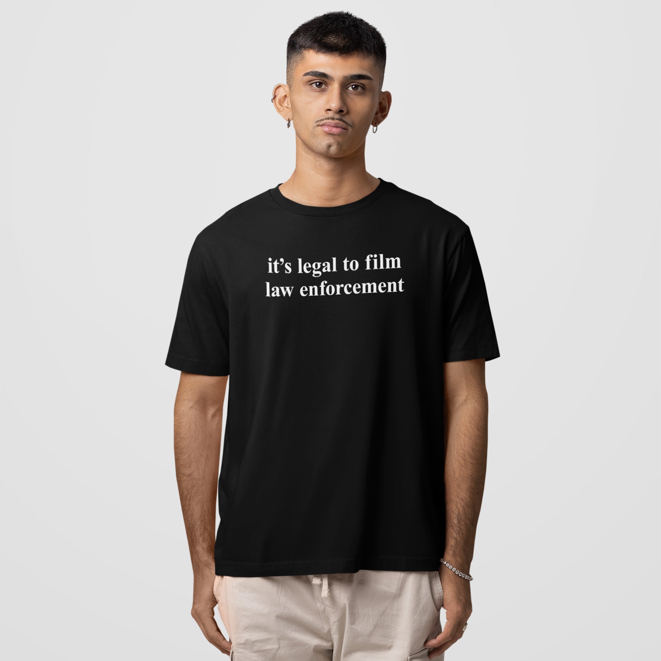 Young man wearing a black Film The Police T-shirt with it's legal to film law enforcement text, paired with light-colored casual pants, embodies a message of activism and awareness.