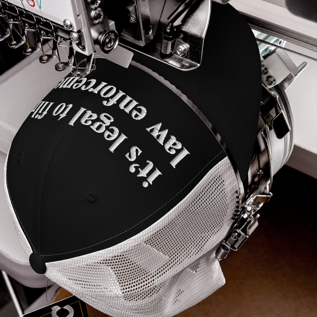 Film The Police Hat in an industrial embroidery machine, stitching white text “It’s legal to film law enforcement” on a black-front/white-mesh trucker cap, highlighting accountability and rights advocacy.