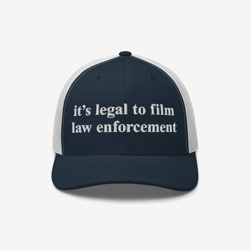 Navy-blue and white mesh trucker cap with “it’s legal to film law enforcement” embroidered in white on the front, representing police accountability advocacy.