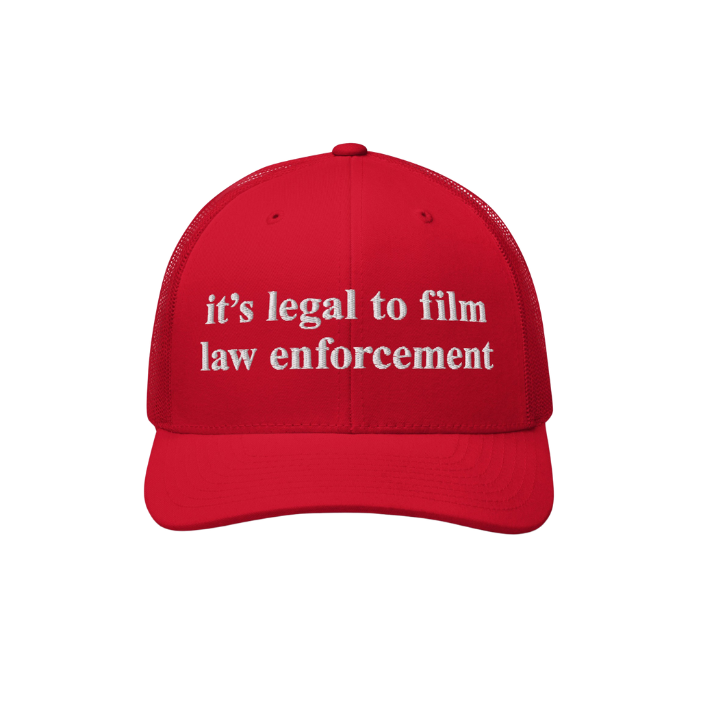 Red mesh-back trucker cap with white embroidered it’s legal to film law enforcement text. The Film The Police Hat embodies 