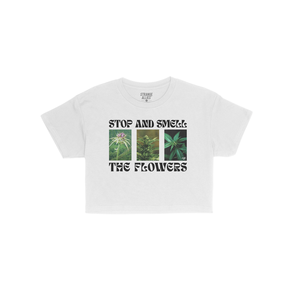Flowers Women's Baby Tee featuring STOP AND SMELL THE FLOWERS text with three cannabis plant photos, capturing a playful blen