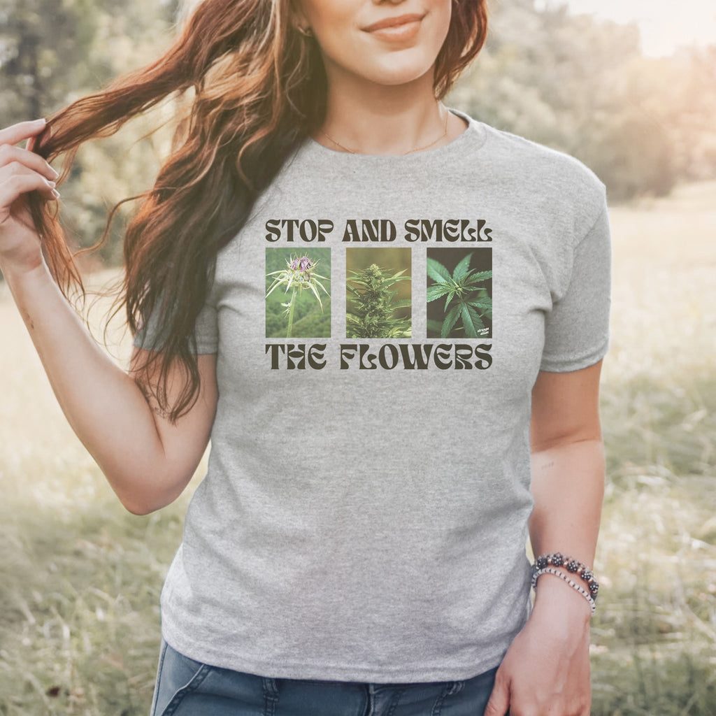 The Flowers Women's Baby Tee features a playful three-panel cannabis graphic with the slogan “STOP AND SMELL THE FLOWERS,” blending humor and botanical appreciation for those who value self-care and individuality.