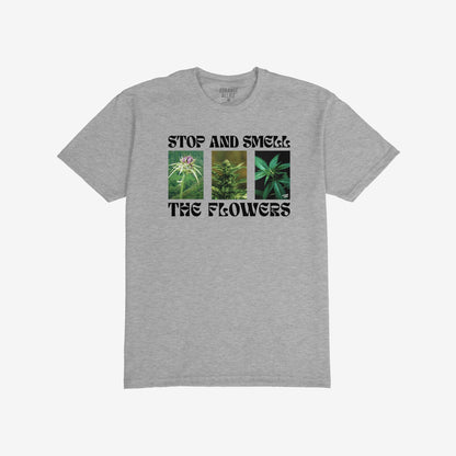 Flowers T-shirt featuring three vertical cannabis images and the slogan “STOP AND SMELL THE FLOWERS” in bold black type, reflecting a playful and rebellious spirit. Brand name “STRANGE ALLIES” inside collar.