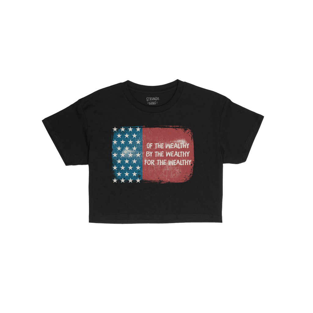 For The Wealthy Women's Baby Tee displays a tattered U.S. flag graphic with the phrase Of the wealthy, by the wealthy, for th