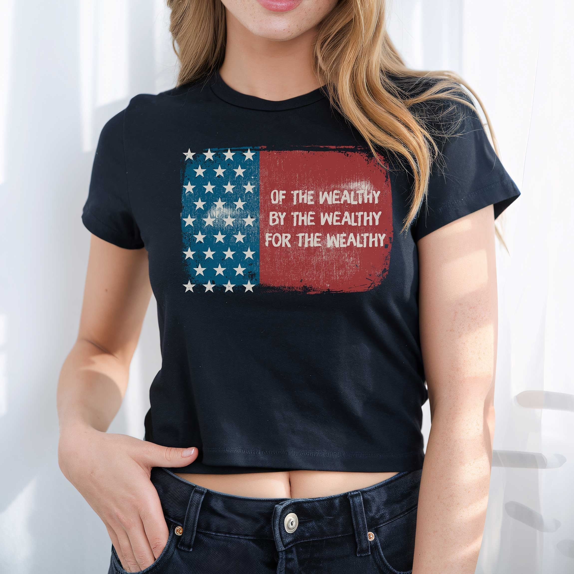 For The Wealthy Women's Baby Tee features a distressed U.S. flag graphic with a bold slogan, embodying a sharp, socio-political statement. The cropped cut accentuates a retro Y2K aesthetic.