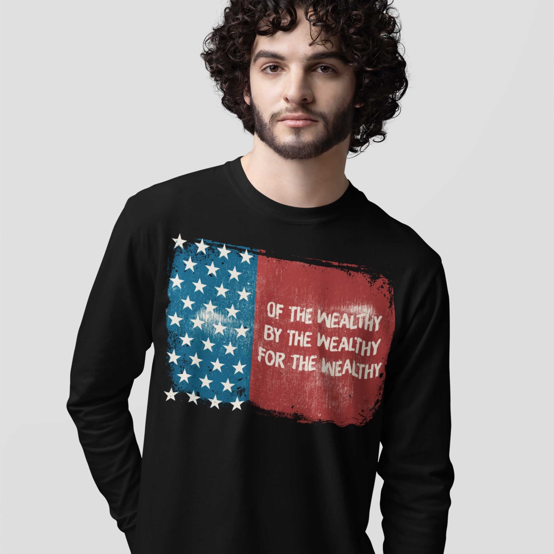 Young man with dark curls models the For The Wealthy T-shirt, featuring a distressed U.S. flag and the bold statement: OF THE WEALTHY, BY THE WEALTHY, FOR THE WEALTHY.