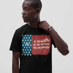 A dark-skinned male model wears the For The Wealthy T-shirt, featuring a distressed American flag and protest slogan. He accessorizes with a hoop earring and braided bracelet, embodying bold activism.