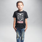 Young boy wearing the Free Palestine JULZ T-shirt, featuring a stylized graphic of eyes and scarf with FREE below, embodying activist support for Palestinian freedom. Paired with blue jeans against a light-gray backdrop.