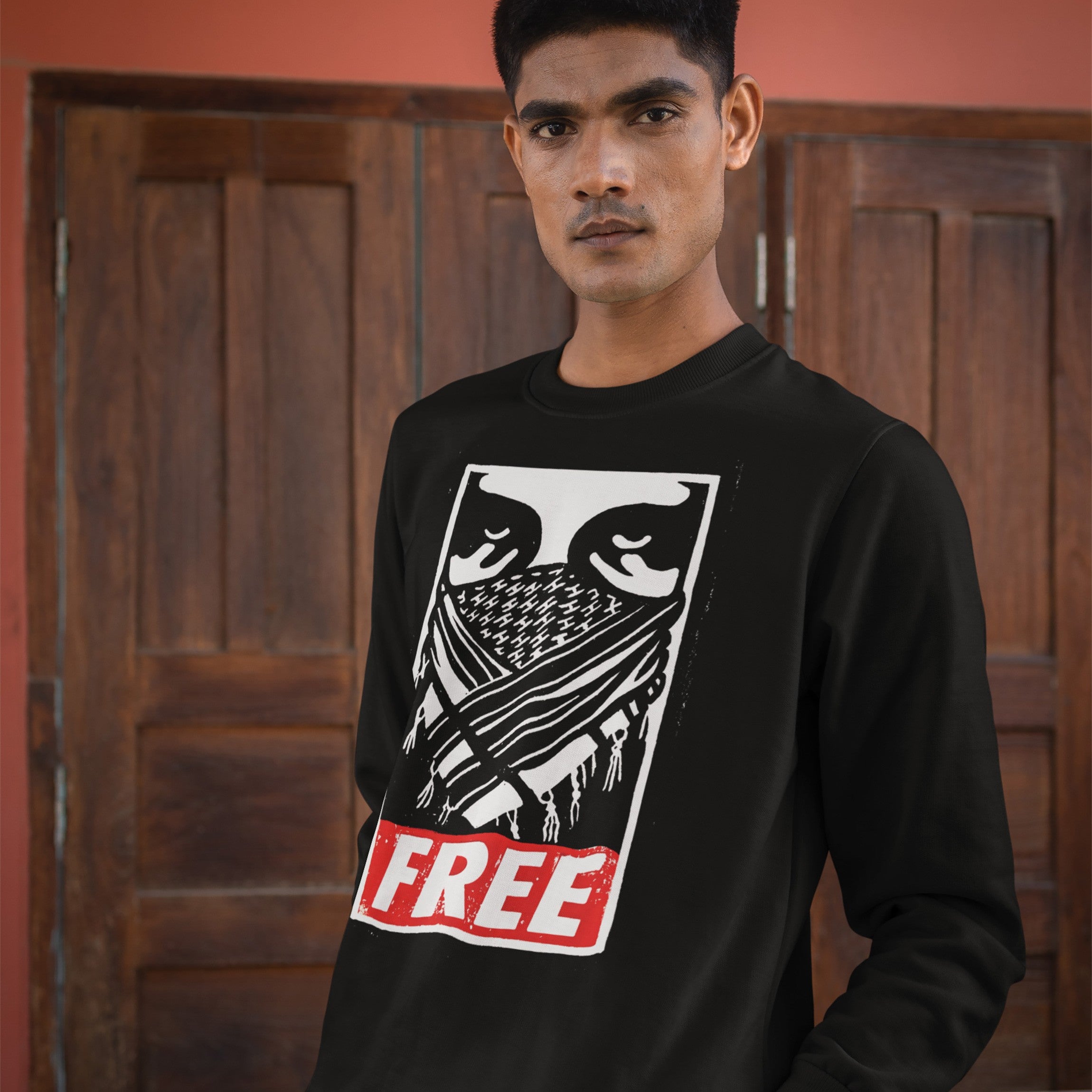 Young man wearing the Free Palestine JULZ Sweatshirt, featuring bold graphic eyes, a criss-cross pattern, and FREE lettering, symbolizing solidarity with Palestinian freedom.