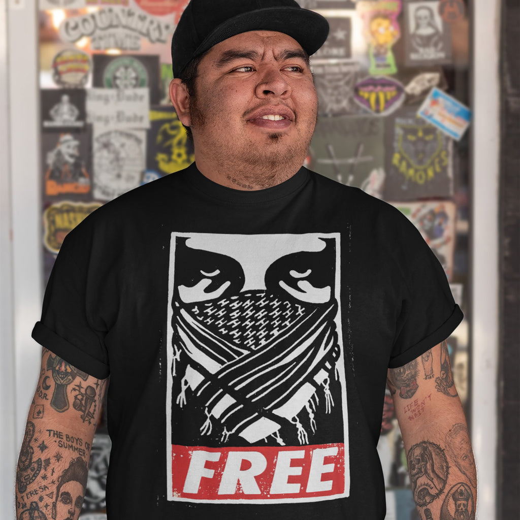 Man wearing Free Palestine JULZ T-shirt featuring narrowed eyes and bandana graphic, with FREE in distressed red letters. Shirt reflects activist spirit, supporting freedom and human rights.